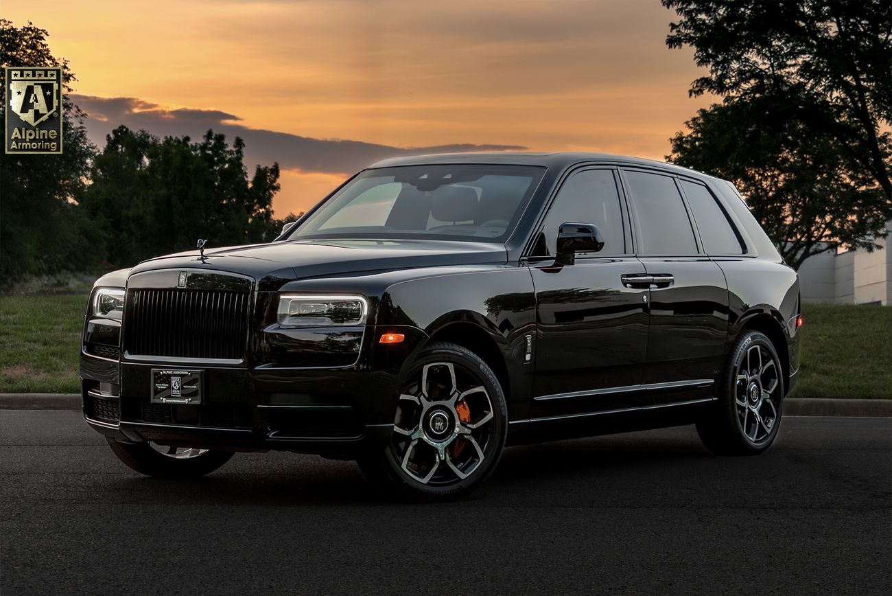 Black Armored Rolls-Royce Cullinan SUV with Spirit of Ecstasy hood ornament and distinctive wheel design, photographed at sunset with trees in background
