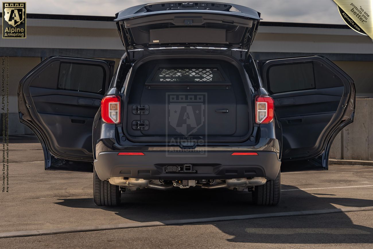 A Ford Explorer PPV with rear and side doors open, showcasing the storage and cargo area. The vehicle is in a parking area with a building in the background.