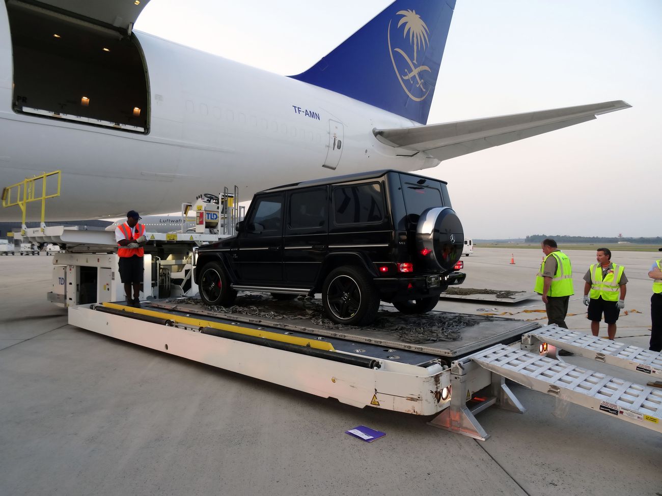 A black SUV from Alpine Armoring being loaded onto a cargo plane by ground crew members. 