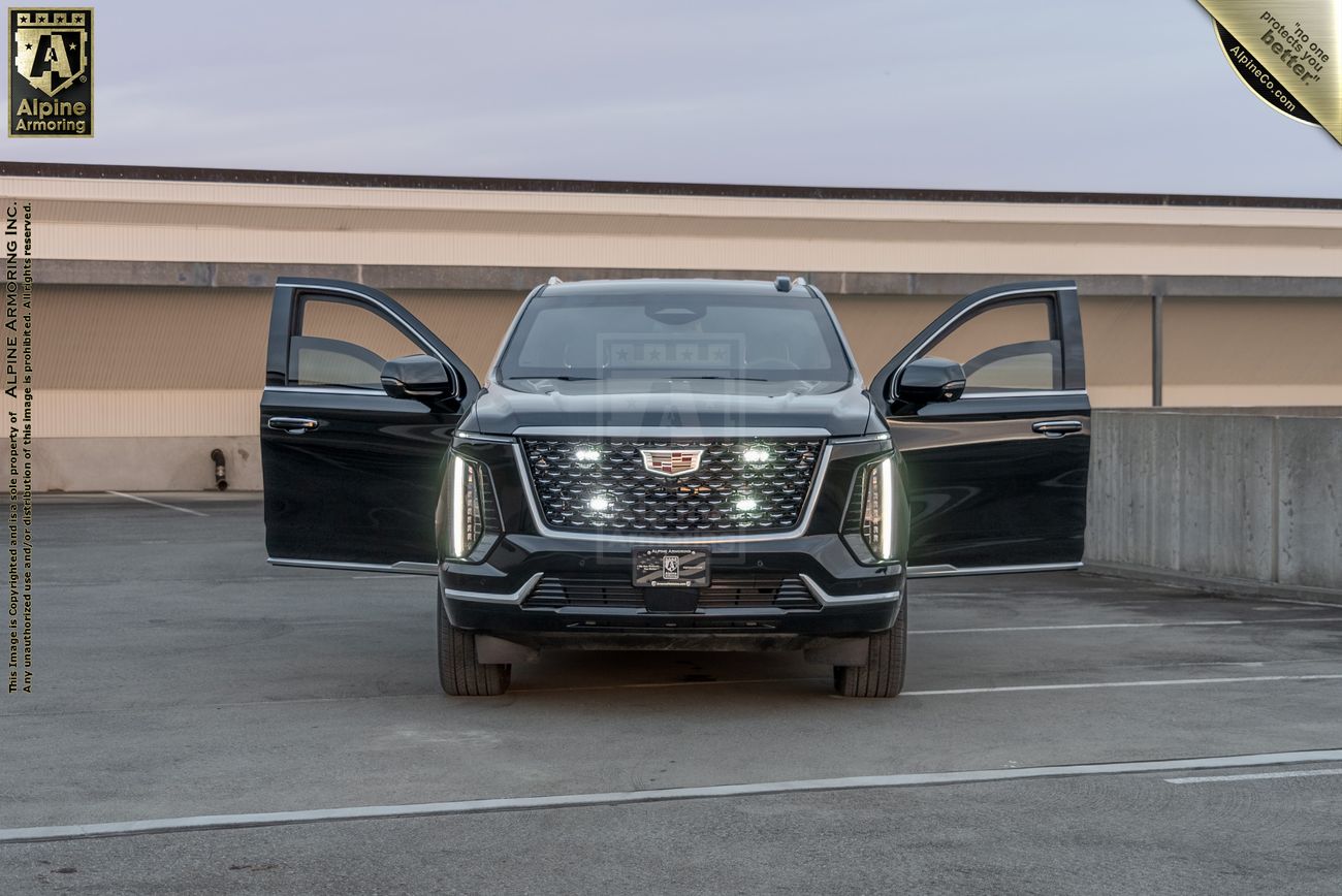 Black Cadillac Escalade ESV Sport with front doors open, parked in concrete parking structure, showing distinctive LED light bar and bold grille.