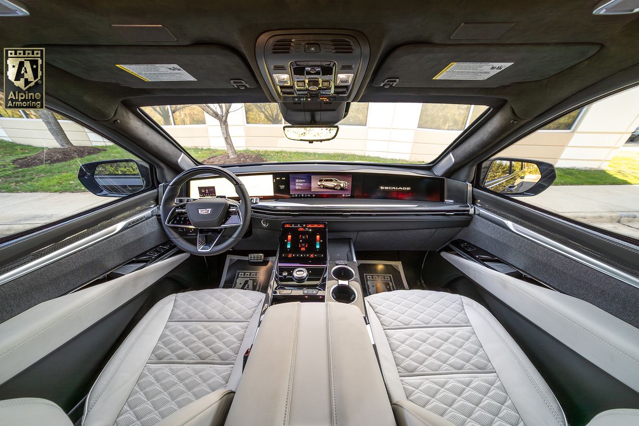 Interior view of an armored Cadillac Escalade SUV showing white quilted leather seats, panoramic sunroof, digital dashboard display, and premium center console