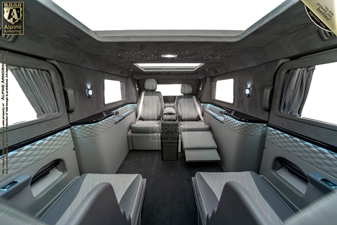 Alpine Armoring Armored Condor® SUV interior with gray and blue quilted leather seating, facing bench seats, privacy curtains, and ambient lighting.