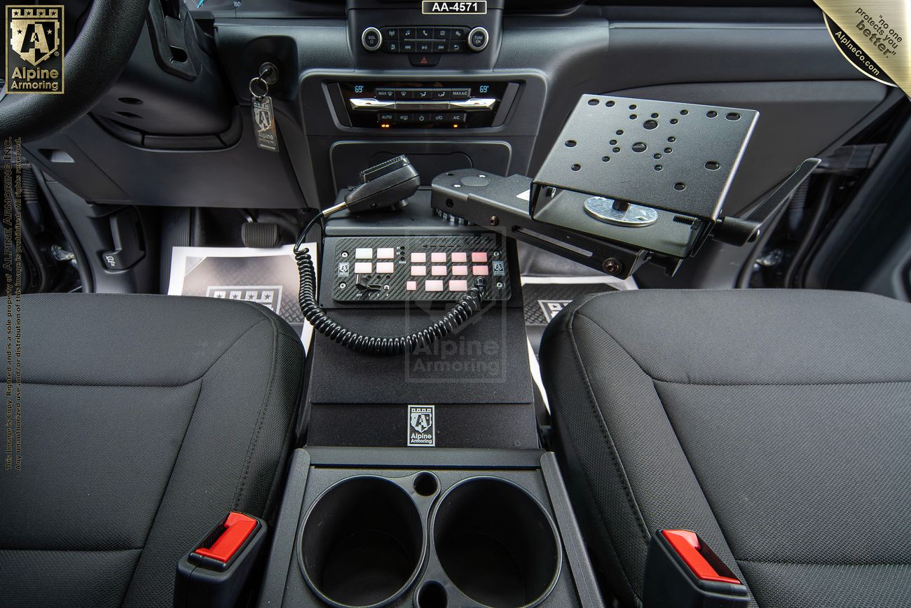 Interior of a Ford Explorer PPV showing the front seats, a center console with cup holders, a mounted tablet holder, and a control panel with buttons and a microphone, likely for communication purposes.