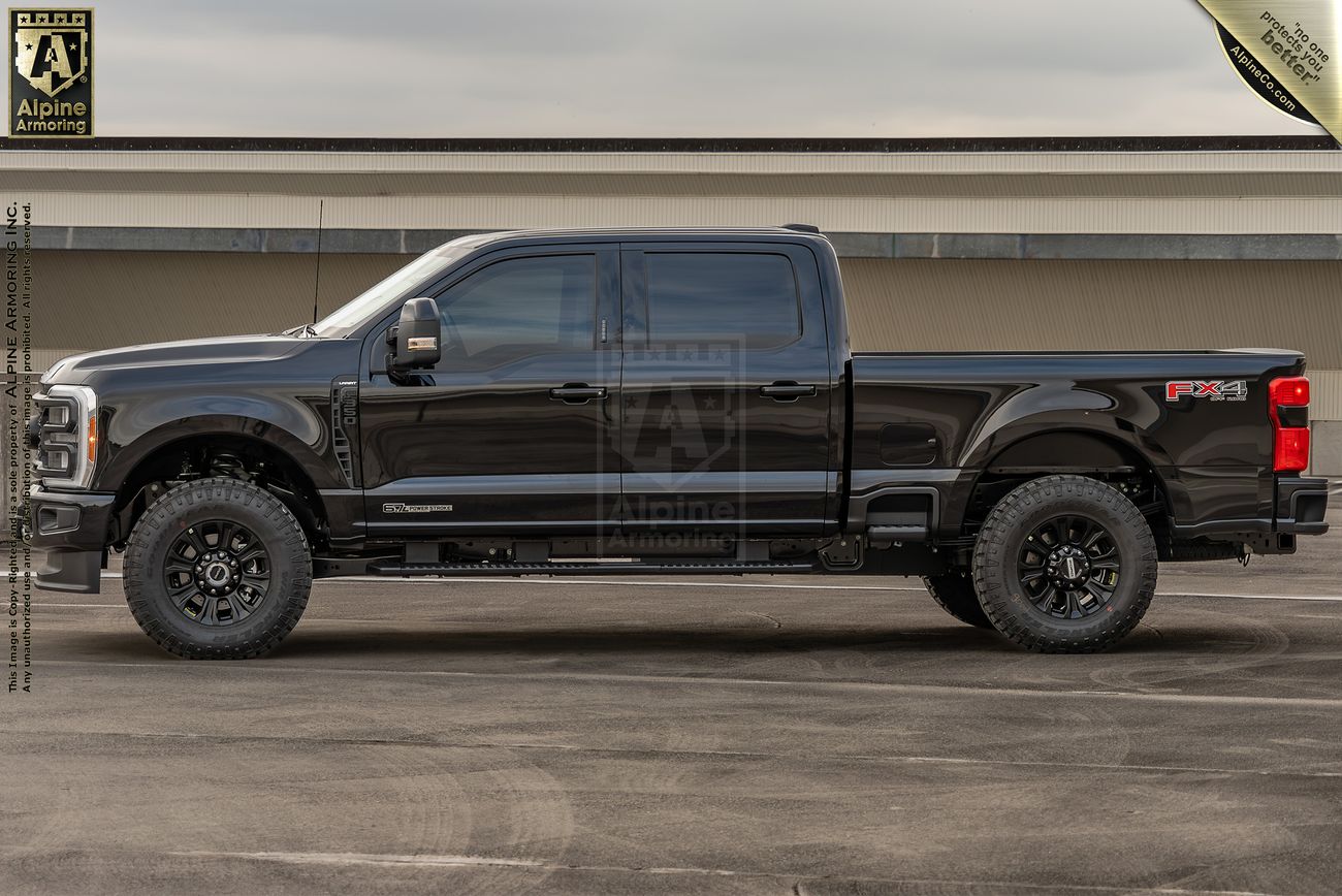 A black Ford F-350 truck with large off-road tires and a lifted suspension is parked on a concrete surface in front of a building.
