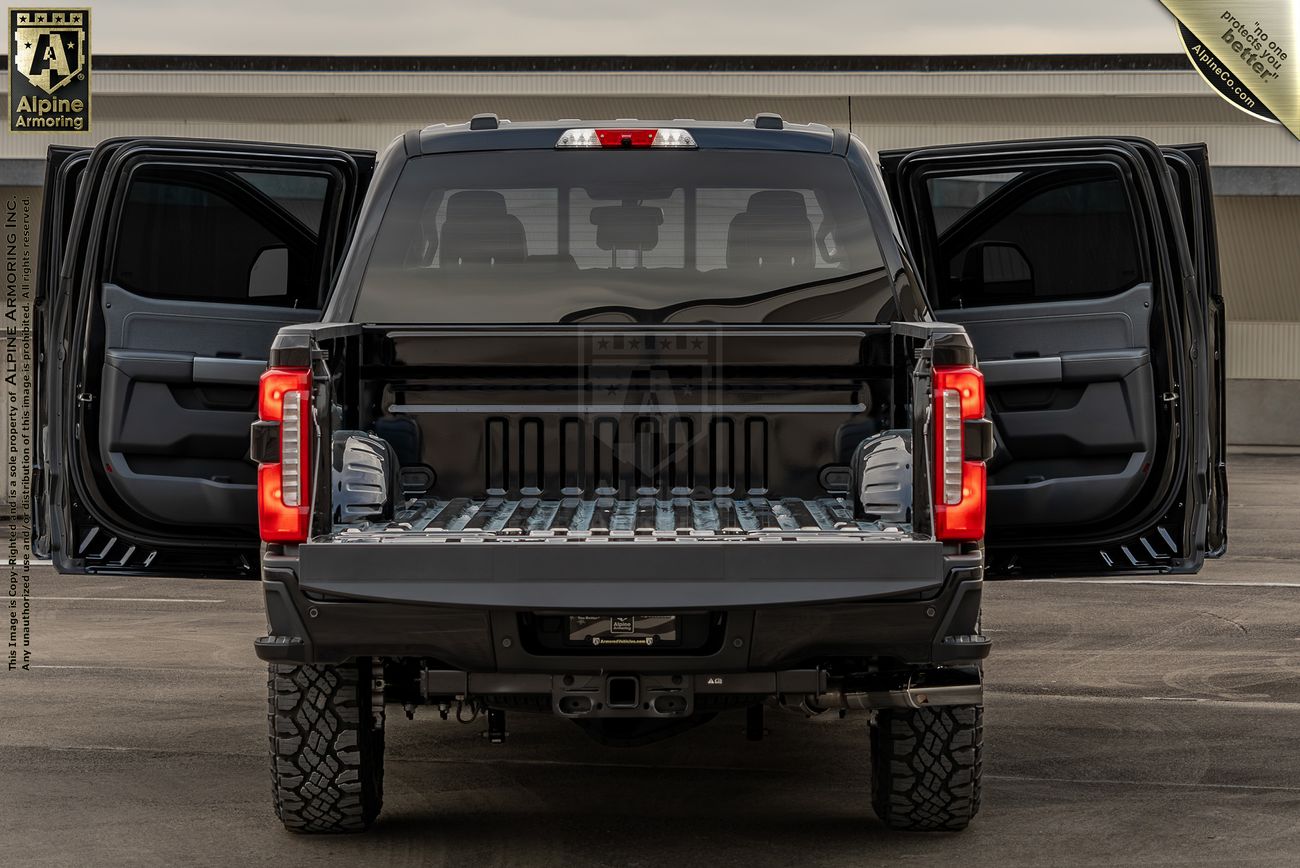 Rear view of a black Ford F-350 truck with its tailgate and rear doors open, showcasing the spacious cargo area. The truck is parked on a paved surface with a building in the background.