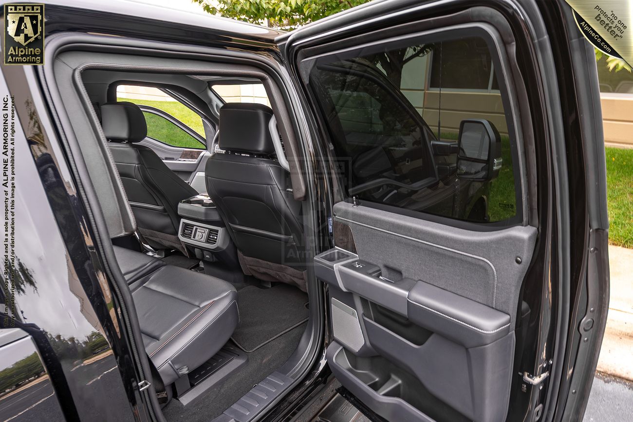 The image shows the open rear passenger door of a black Ford F-350. The interior features black leather seats and a view of the front seats. Some greenery and a building are visible outside.