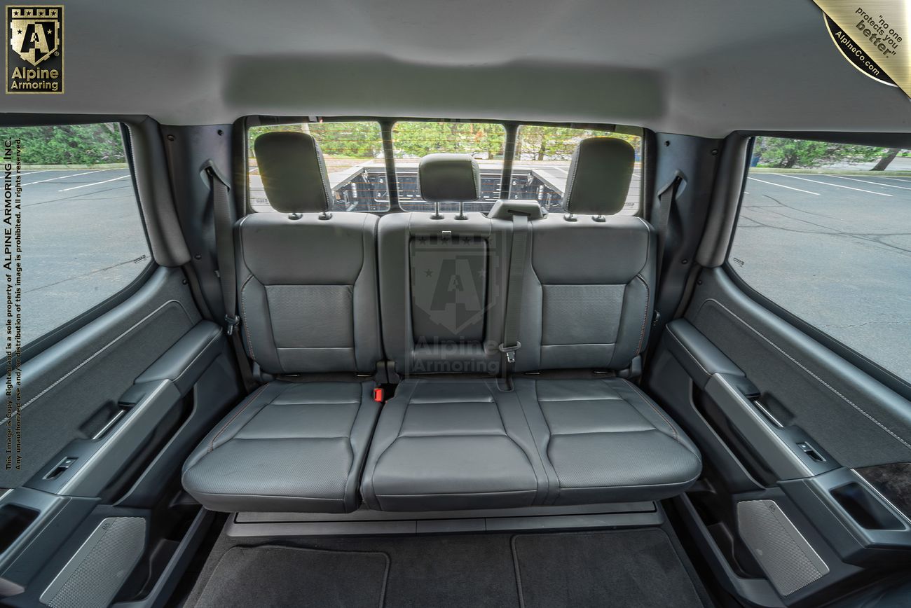 Interior view of an Ford F350 showcasing three rows of black leather seats, with the second and third rows visible. The vehicle is parked in an empty outdoor area, seen through the rear windows.