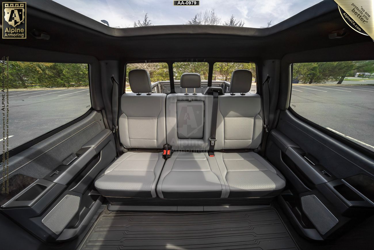 Interior of an armored Ford Lightning showcasing a spacious backseat with three leather seats, a central fold-down armrest, and large windows, offering an open view of the parking area outside.