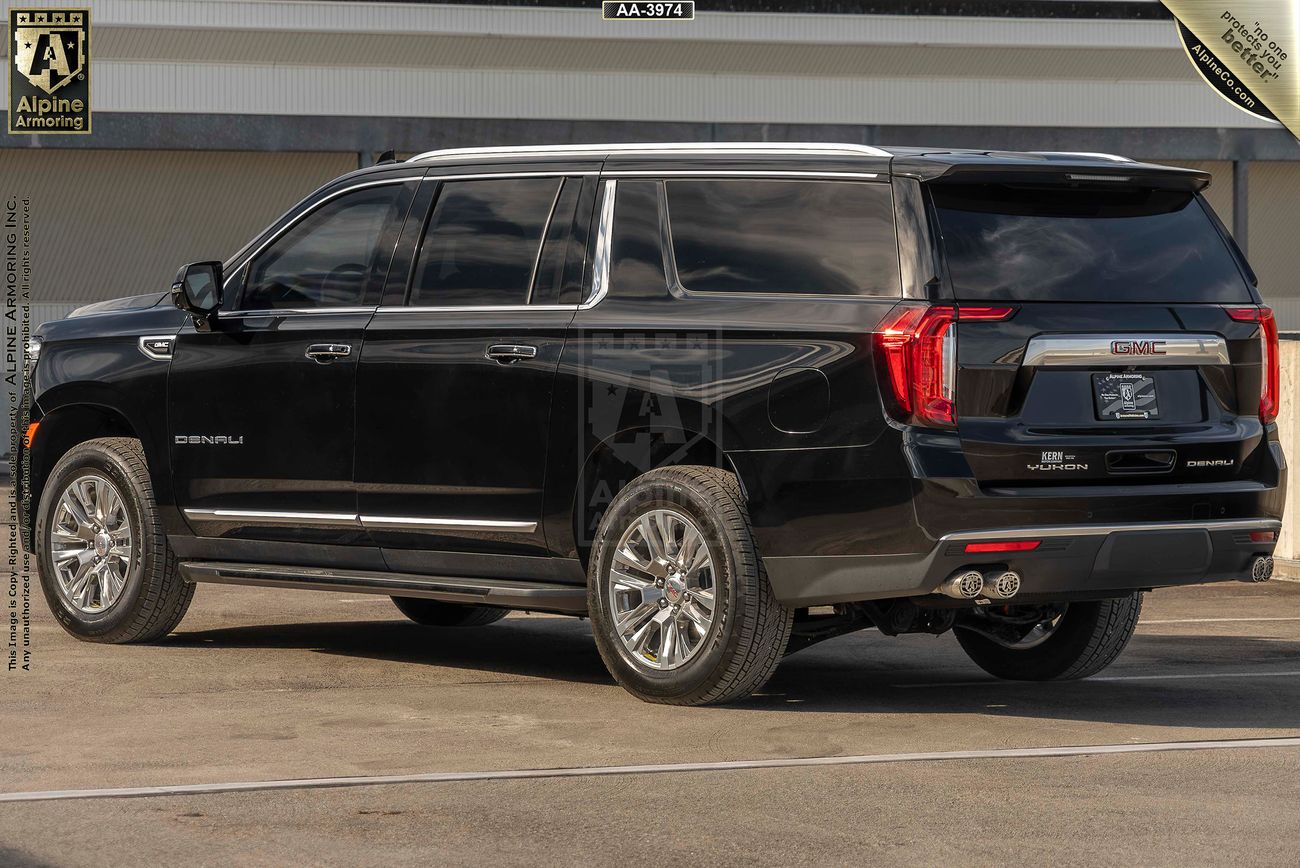 A black armored GMC Yukon Denali SUV is parked on a concrete surface. The vehicle is viewed from the rear.