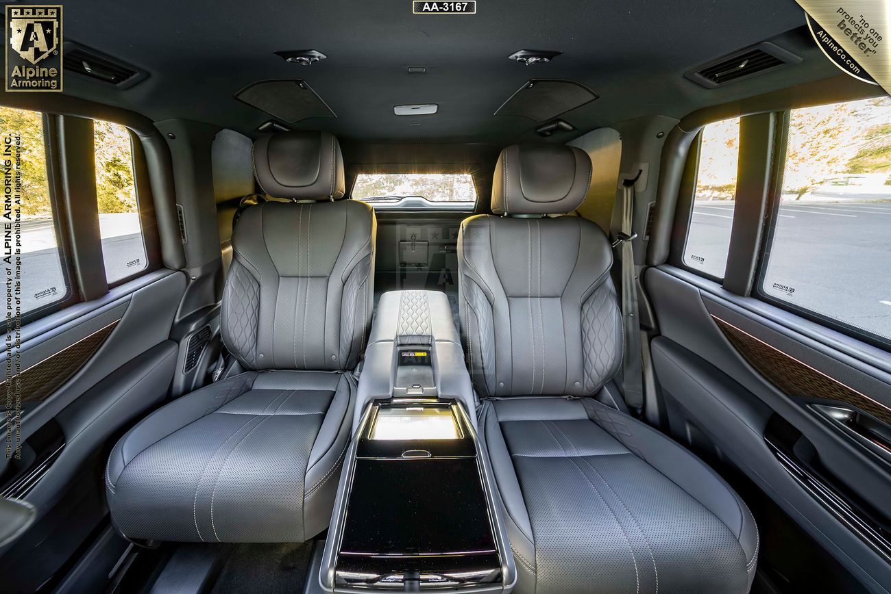 Interior of a Lexus LX 600 Ultra Luxury featuring two grey leather rear seats with a central console, wood-paneled accents, and large windows.