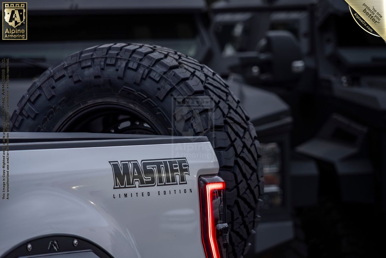 Close-up of the rear of a white Mastiff Limited Edition truck, with a large spare tire mounted on the back and another black vehicle partly visible in the background.