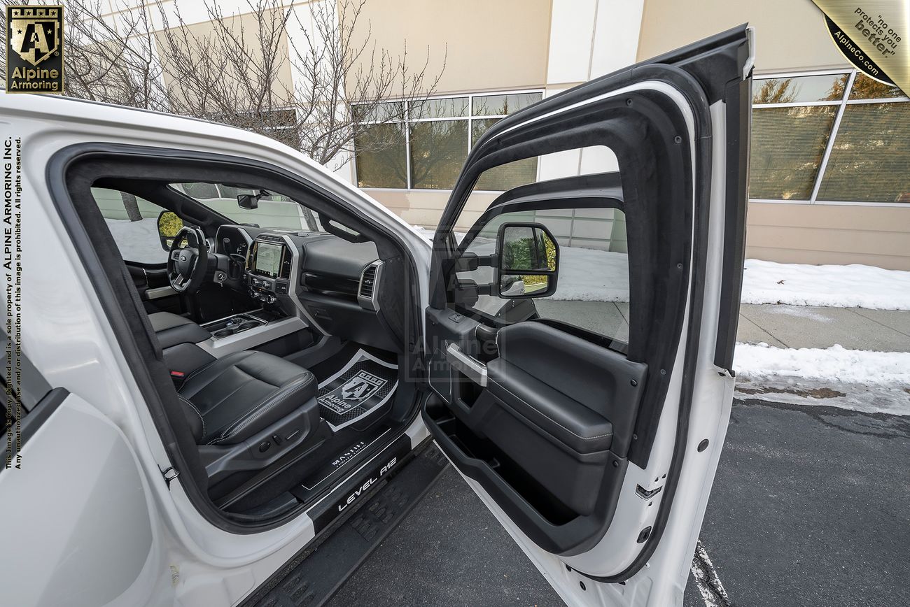 An open passenger door shows the interior of a white Mastiff parked outdoors near a snowy sidewalk, with visible trees and a building exterior in the background.