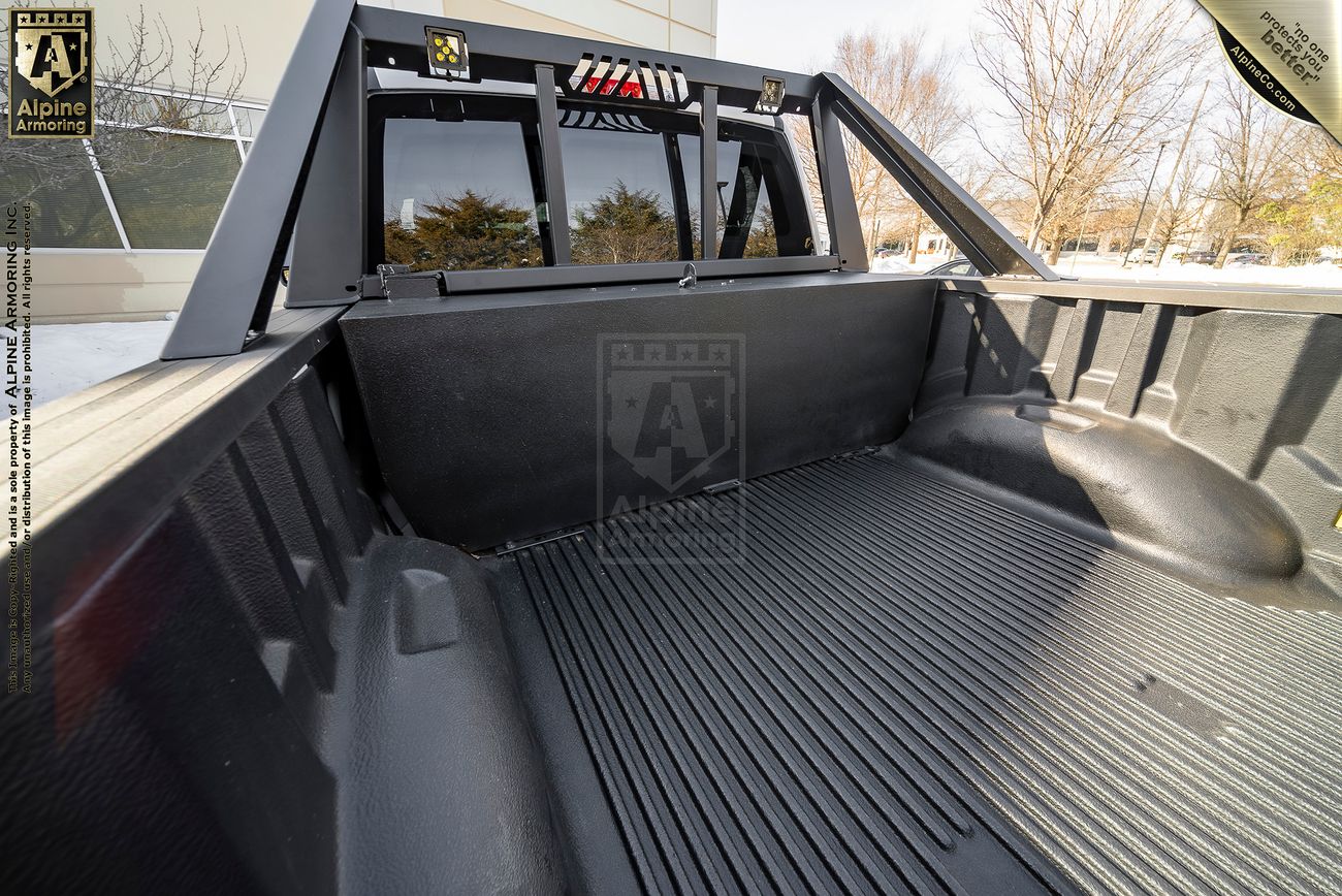 View of an empty Mastiff truck bed with a black liner and a sturdy roll bar, parked outdoors with a building and trees in the background.