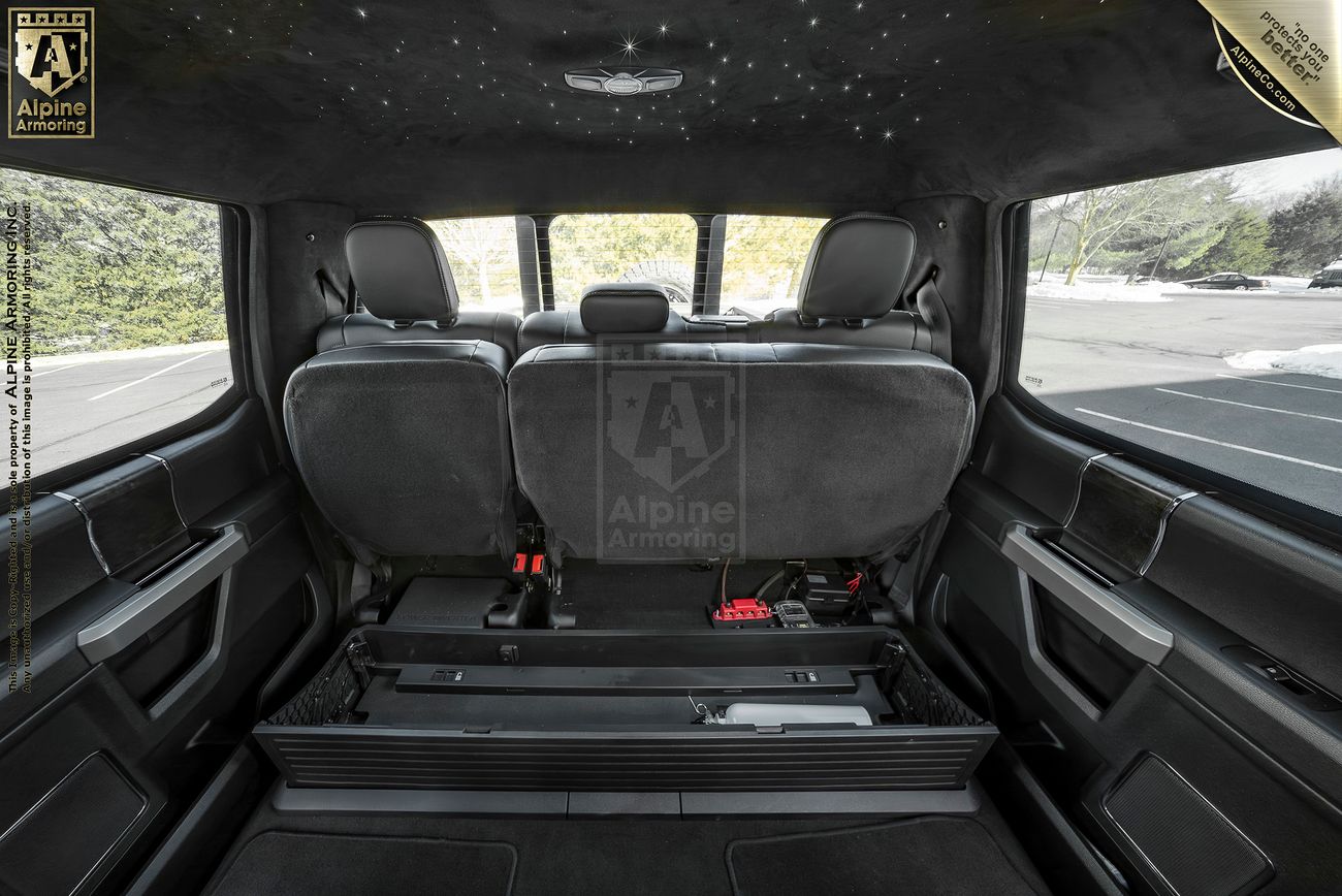 The interior of a Mastiff with the rear seats folded and a protective barrier in place. The vehicle features a label indicating Alpine Armoring on the inside.