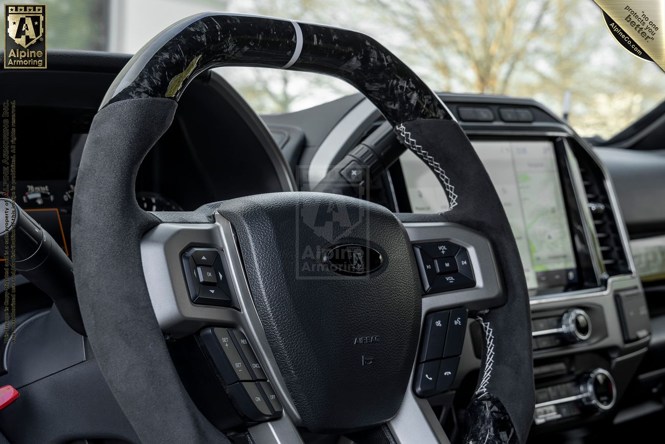 Interior view of a Mastiff showing a close-up of a steering wheel and dashboard, featuring a touchscreen display with a map. The steering wheel is covered with a combination of materials.