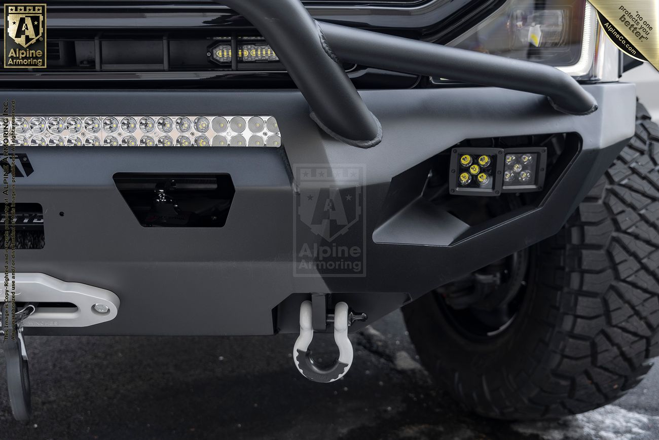 Front view of a Mastiff's rugged bumper with an integrated winch, multiple LED lights, and a towing hook. The vehicle also has large off-road tires.