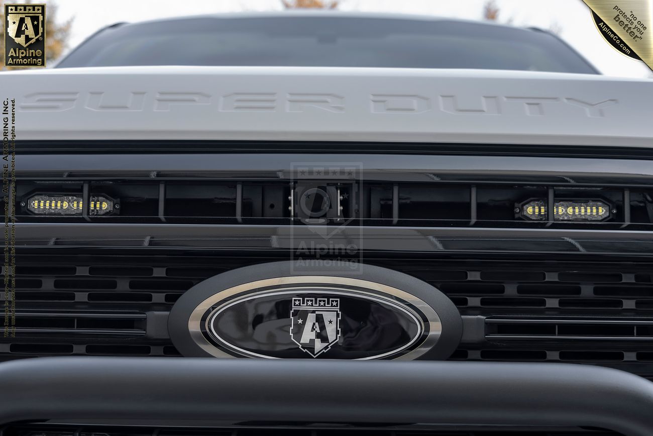 Close-up of a Mastiff's front grille featuring embedded LED lights  with a "Super Duty" engraving above the grille and Alpine Armoring insignia on the vehicle.