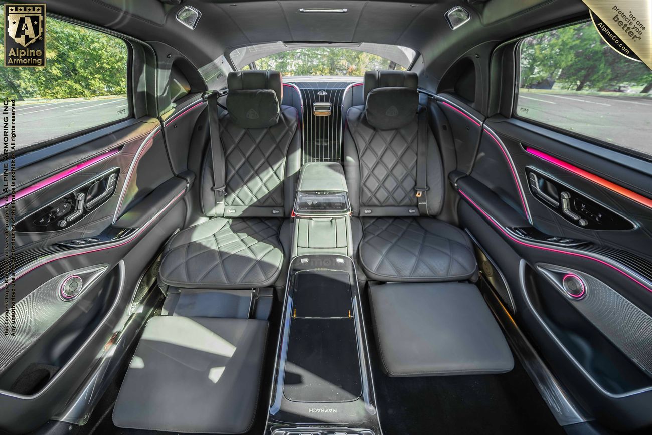 A black armored Mercedes Maybach S 580 sedan interior featuring diamond-stitched black leather seats, ambient LED lighting, and an extended center console with multiple control panels and compartments.
