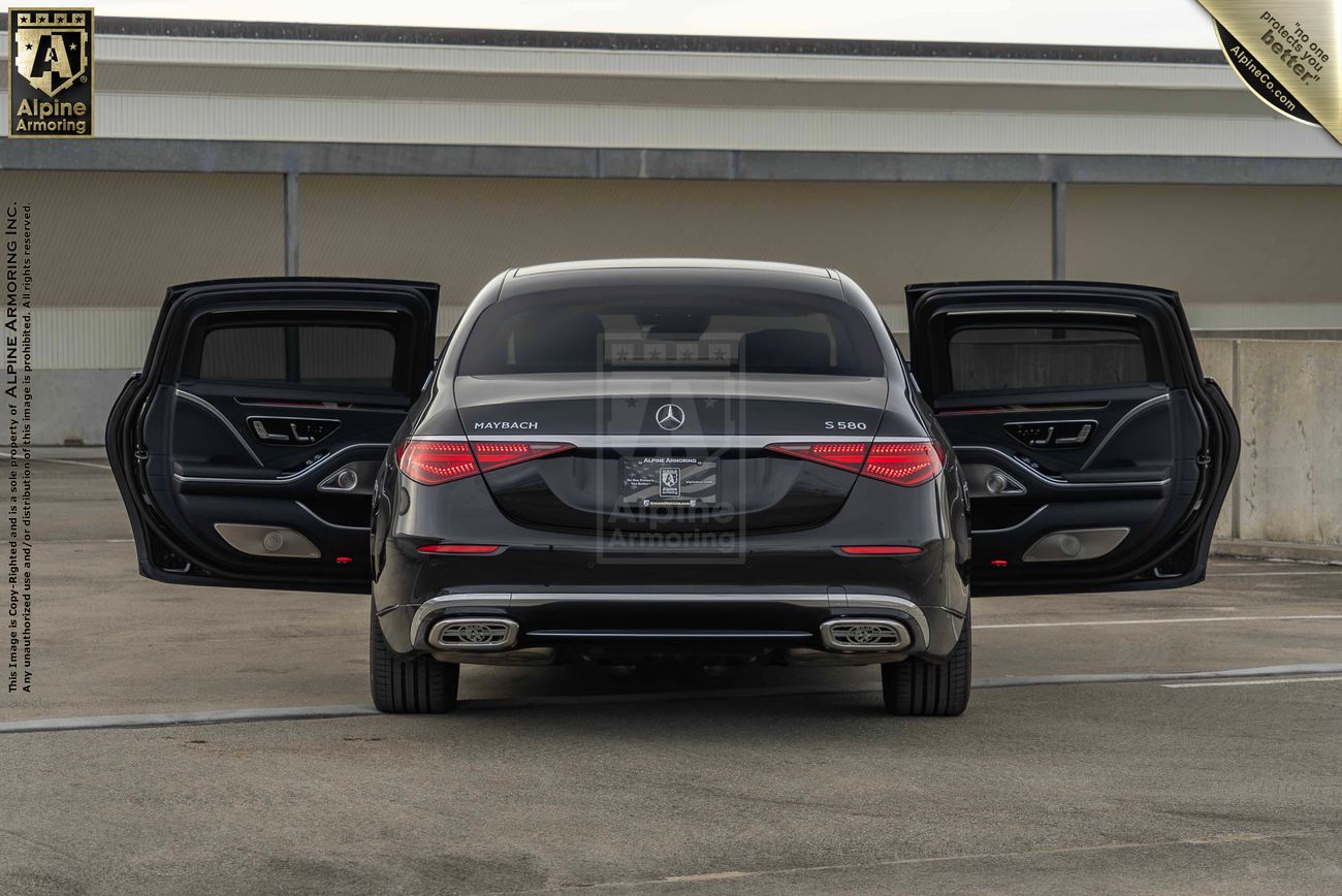 A black armored Mercedes Maybach sedan with open rear suicide doors is parked on a concrete surface in front of a building. The car has "Maybach S680" and "4MATIC" badges on the back.