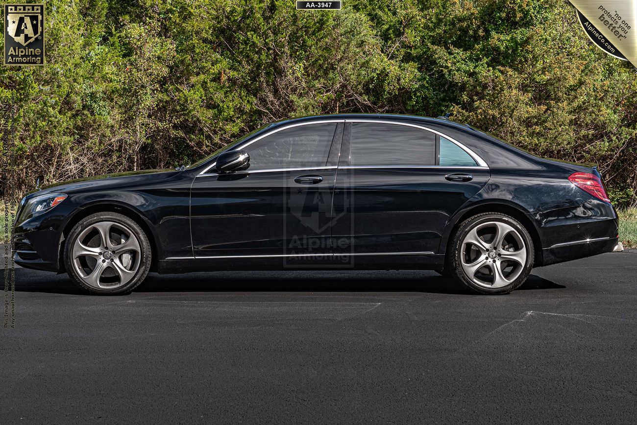 Side view of an armored black Mercedes S550 parked on a paved surface, with trees in the background.