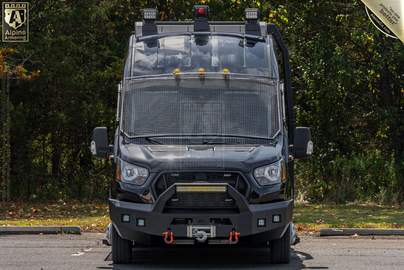 A black tactical Pointer van with reinforced front, mounted lights, and a winch, parked on a paved area with a forested background. Badges on the top corners of the image mention "Alpine Armoring" and a certification.