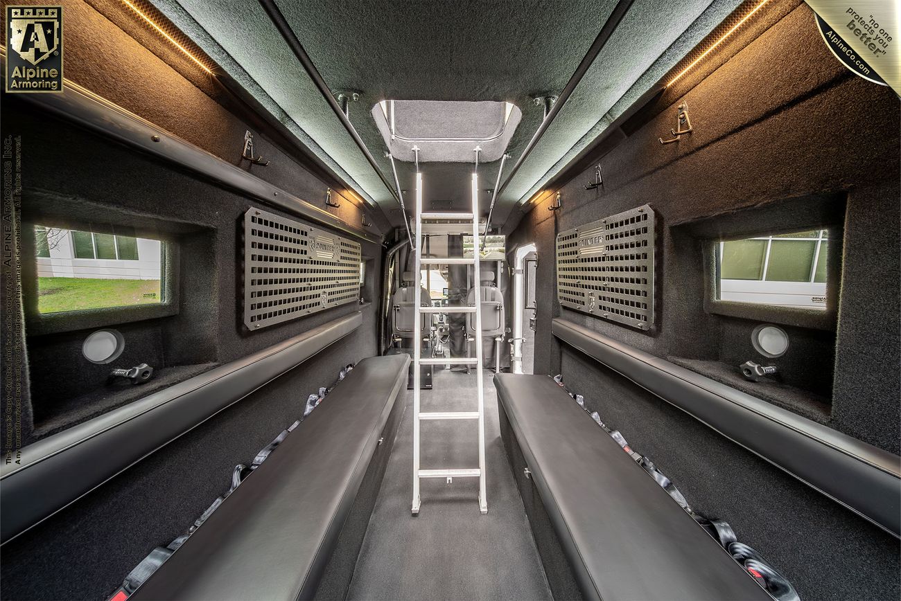 The interior of a black armored SWAT van, known as the Armored Pointer from Alpine Armoring, with the interior ladder set up showcasing reinforced windows, tactical lighting, and advanced security features. 