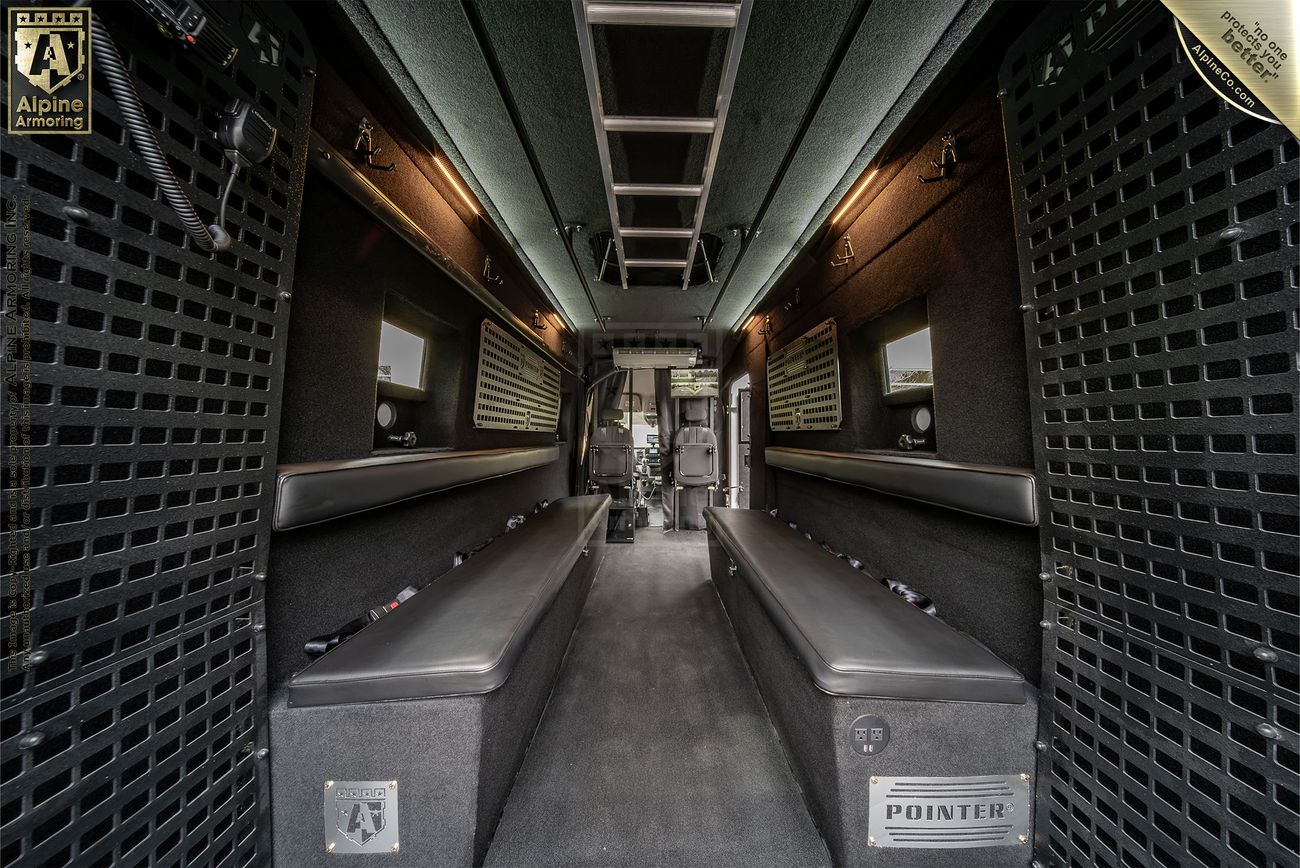 Interior of a Pointer van with padded benches on both sides, a central aisle, and equipment storage compartments on the walls. 