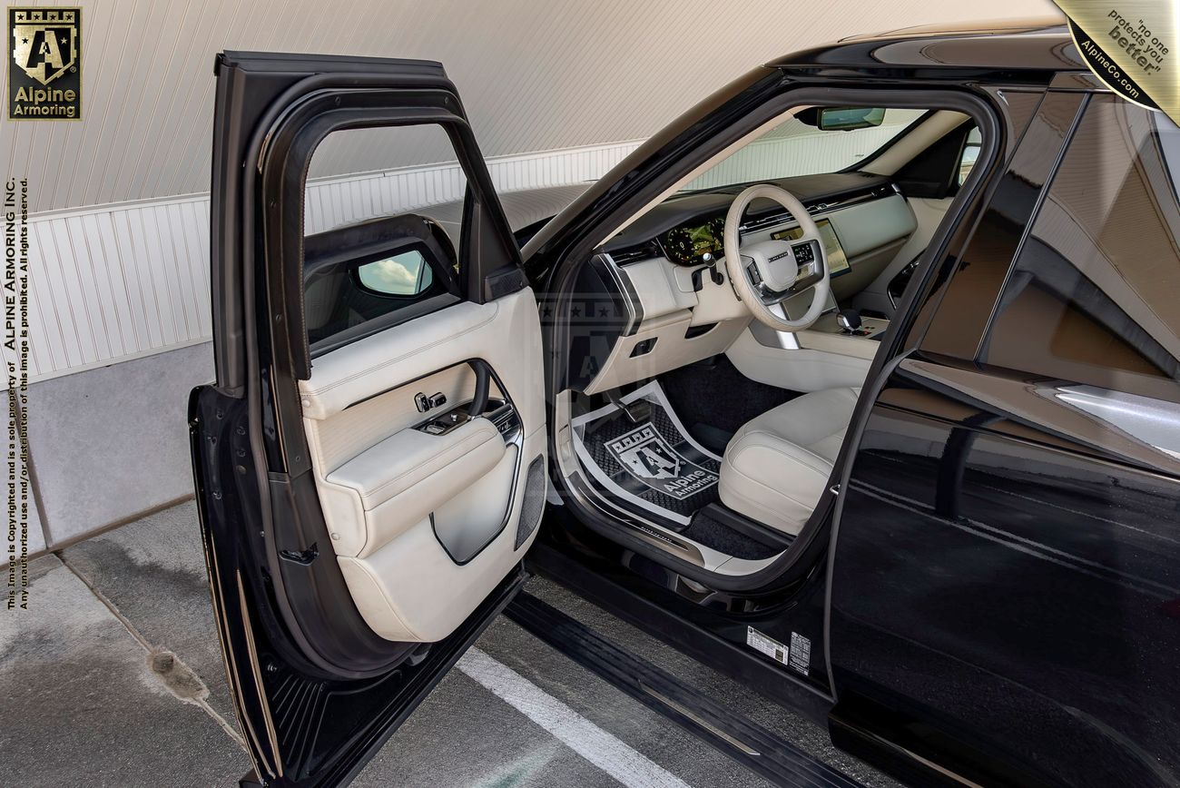 Range Rover Autobiography interior with front doors open, showing cream and navy blue leather seats, wood trim dashboard, and light-colored upholstery.