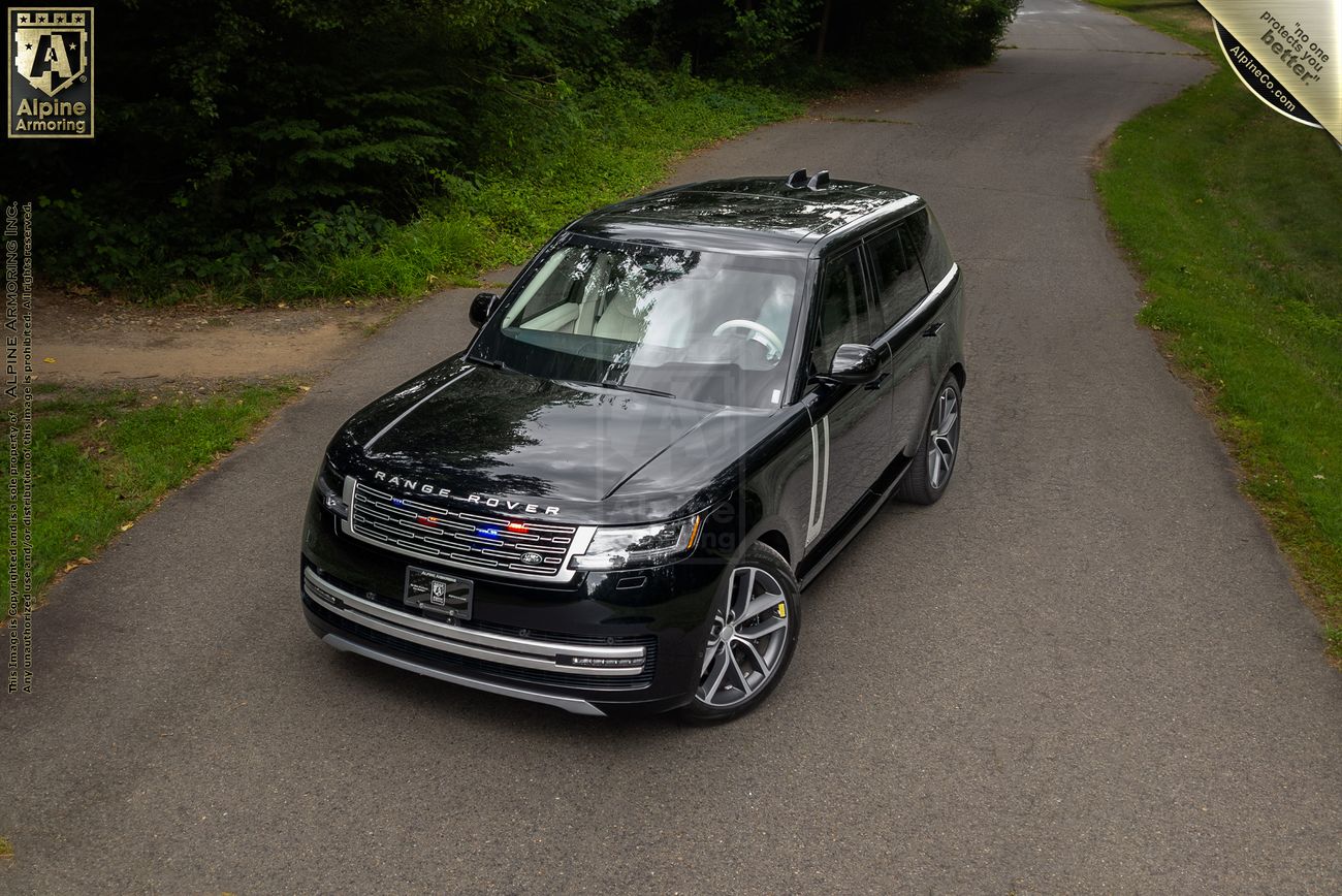 Black Range Rover Autobiography SUV with panoramic sunroof on tree-lined road, viewed from above showing distinctive two-tone roof design.