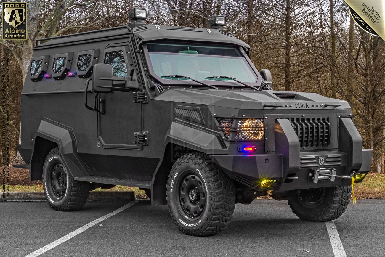 A black, bulletproof armored CUDA is parked in an outdoor setting with trees in the background.