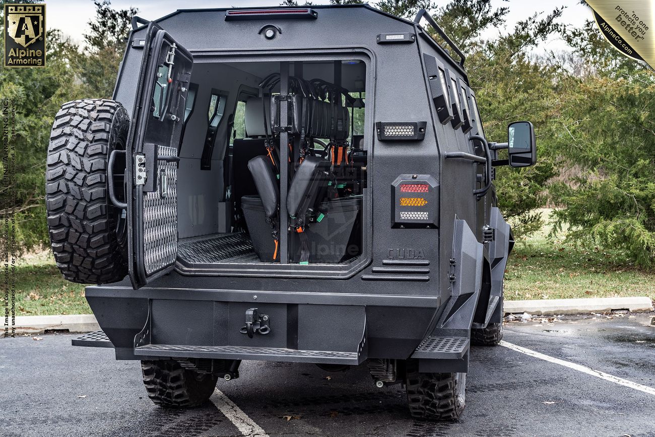 A fortified CUDA is shown from the rear with its doors open, revealing an interior with tactical seating and equipment. The exterior appears robust, designed for off-road and tactical use.