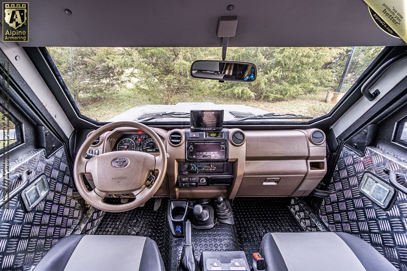 Interior view of a CUDA dashboard showing a steering wheel, control panel, and various devices. The windshield offers a clear view of the trees outside.