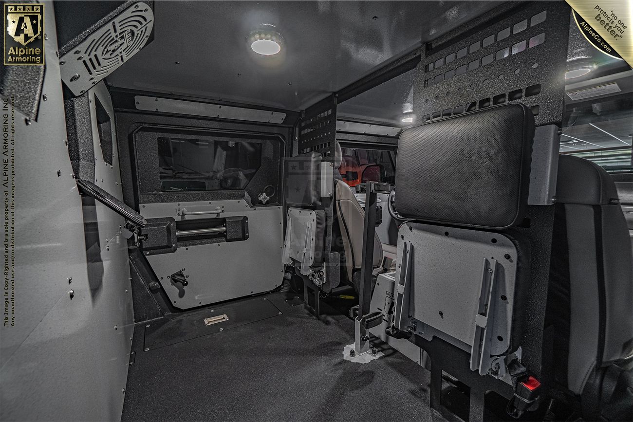 Interior of an armored Pit-Bull VXT from Alpine Armoring showing foldable seating, reinforced walls, and a control panel. The design emphasizes security and functionality.
