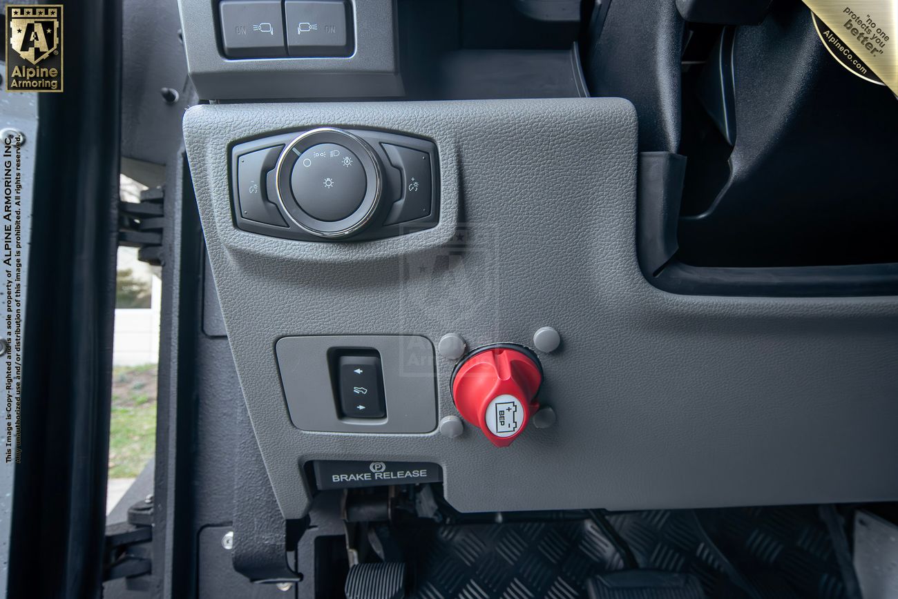 Close-up view of a armored Pit-Bull VX 50 cal dashboard with various controls, including a circular knob, a switch, and a red lever marked with a lock symbol.