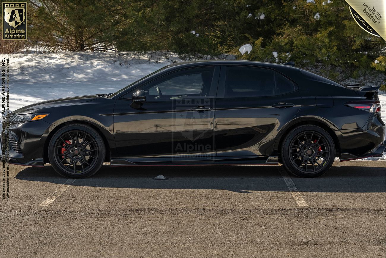 Left side view of an armored Toyota Camry TRD sedan in a snowy environme