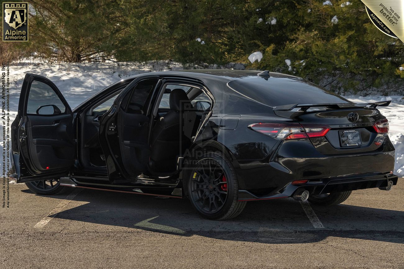 Rear view , from left, with doors open, of an armored Toyota Camry TRD sedan in a snowy environme