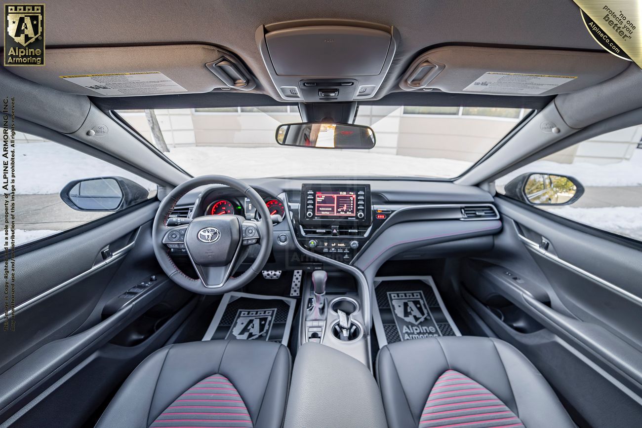 Interior view of a Toyota Camry from Alpine Armoring  showcasing the dashboard, steering wheel, center console, and front seats with Alpine Award recognition plaques visible.