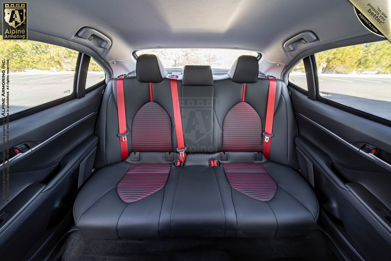 Interior view of the back seat of a  Toyota Camry TRD sedan showing black leather upholstery with red seat belts and red accents on the seats, surrounded by the car's rear windows.