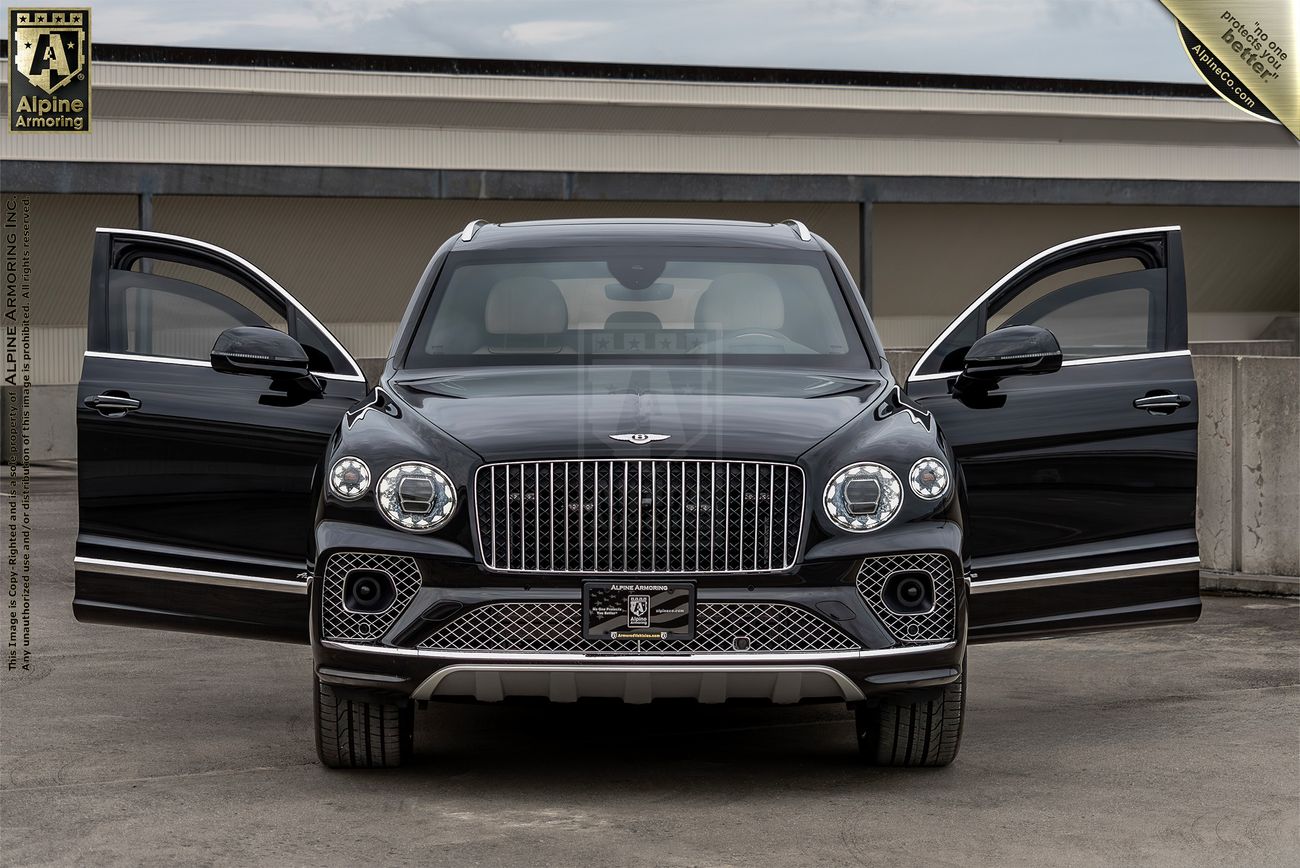 A black armroed Bentley Bentayga luxury SUV is displayed with both its front doors open, showcasing its front grille and detailing. The vehicle is parked on a concrete surface with industrial buildings in the background.
