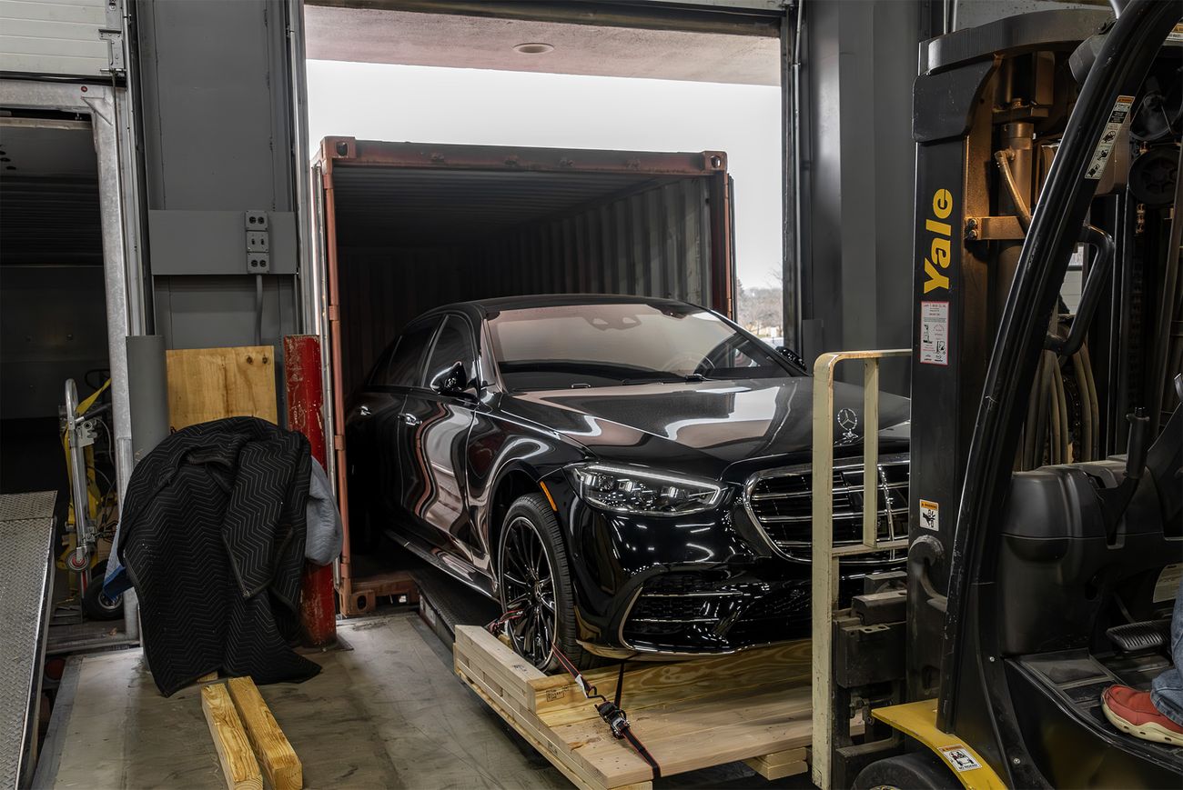 A black Mercedes-Benz car from Alpine Armoring  being loaded into a shipping container with the help of a forklift.
