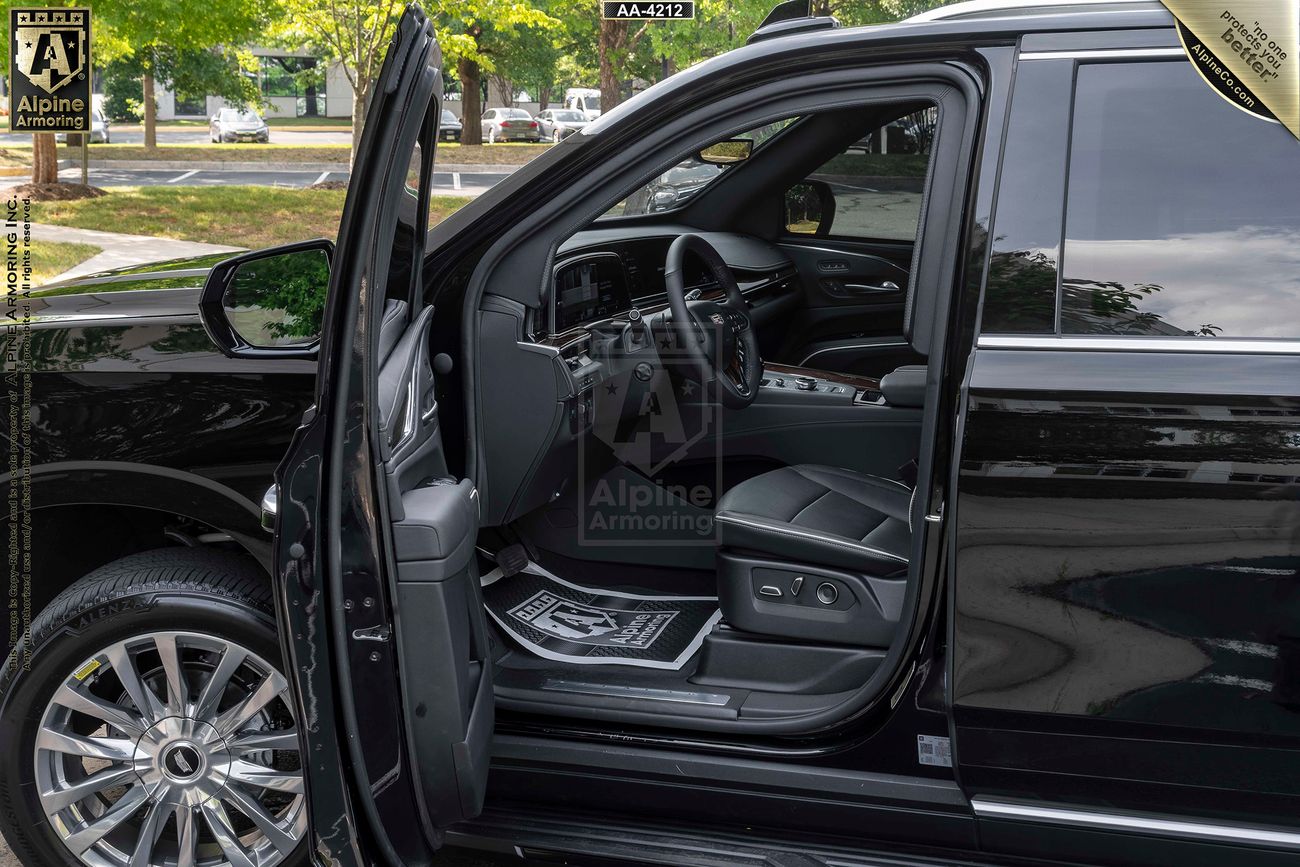 The interior of a black armored Cadillac Escalade ESV with its front and rear doors open, revealing leather seats and an equipped dashboard.