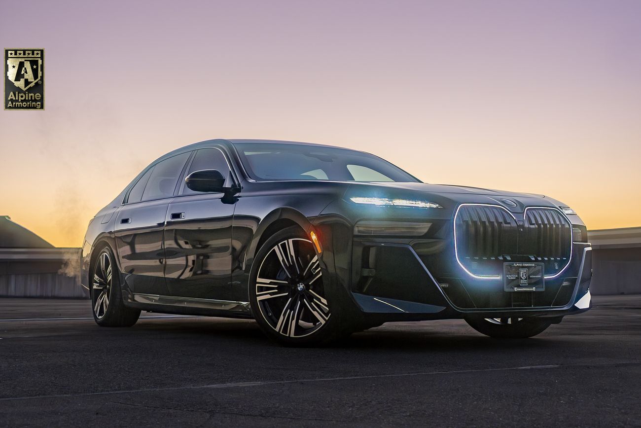 Black armored BMW 7 Series sedan with illuminated kidney grille parked on rooftop at sunset, featuring multi-spoke wheels and Alpine Armoring branding