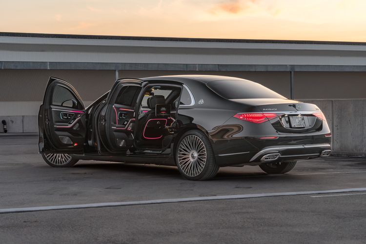 Black Mercedes-Maybach S580 with all four doors open, parked in urban setting at dusk, showing red ambient interior lighting.
