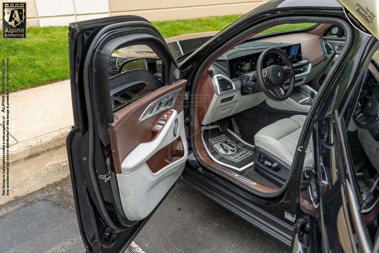 BMW interior with front doors open, showing two-tone brown and cream leather seats, wood trim, and digital dashboard.