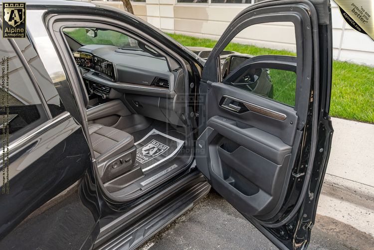 Black Chevrolet Suburban leather interior with front doors open, showing dashboard, center console with rotary controller, and wood trim accents.