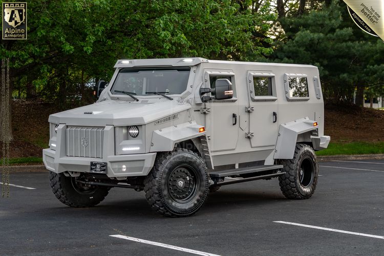 White Alpine Armoring Armored Condor® SUV with reinforced body panels, heavy-duty suspension, and bulletproof windows parked on street with trees in background.