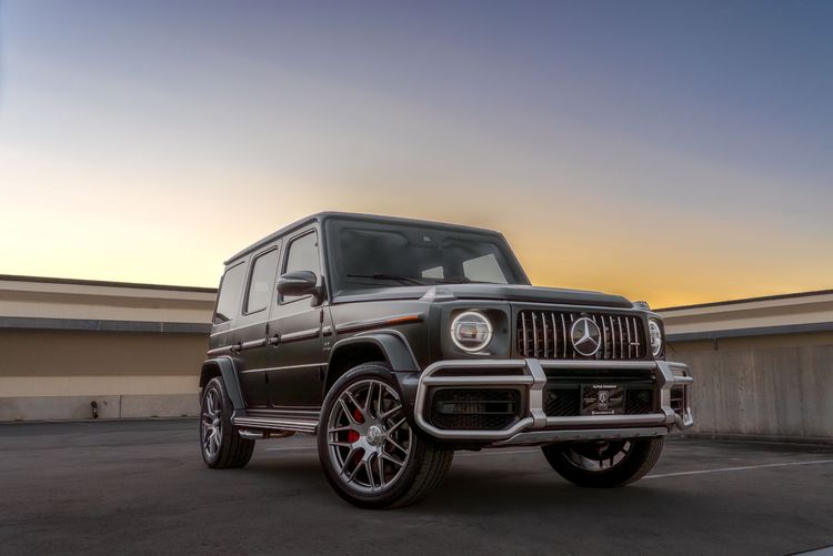 Black Mercedes-AMG G-Wagon with performance wheels and red brake calipers photographed at sunset on concrete structure.