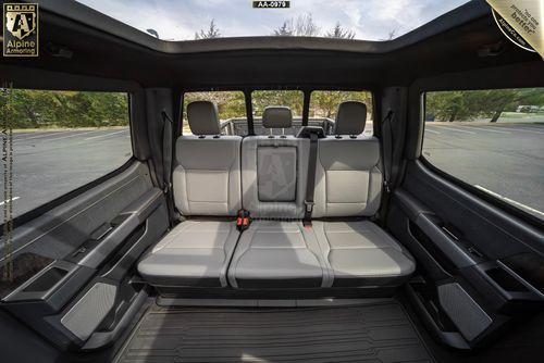 Interior of an armored Ford Lightning showcasing a spacious backseat with three leather seats, a central fold-down armrest, and large windows, offering an open view of the parking area outside.