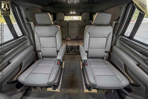 Interior of a GMC armored GMC Yukon Denali XL showing four leather seats, two in the middle row facing forward, and two in the rear. The seats feature armrests, and the car has large windows on the sides.