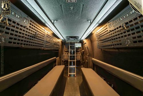 Interior view of a tactical van, a Pointer based on Mercedes Sprinter 3500XD, featuring padded benches, metal panels on the walls, and a central ladder leading to an upper compartment.